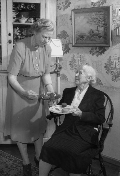 Two women at a meeting of the Madison Home Economics Club with the theme "Good Nutrition, A Wartime Challenge." Nellie Kedzie Jones, guest of honor and past head of the Wisconsin Home Economics Extension, is being served by Mrs. P.A. Hauver, a past president of the Madison Home Economics Club.