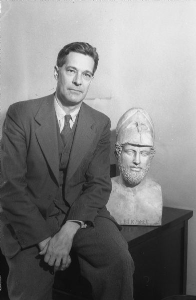 Portrait of Walter R. Agard, professor of Classics at the University of Wisconsin, sitting next to a statue of Pericles.