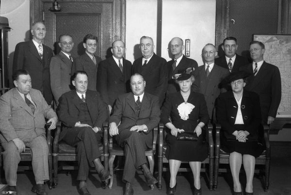 Group portrait of 13 superintendents of state welfare institutions with A.W. Bayley (extreme right, standing), director of the Wisconsin Deptartment of Public Welfare. Sitting, left to right: Dr. M.K. Green, head of Mendota State Hospital; B.P. Kraemer, Green Bay State Reformatory; T.R. Uthus, Waukesha Industrial School for Boys; Ethel Brubaker, Oregon Industrial School for Girls; Mrs. Marcia Simpson, Taycheedah Prison and Industrial Home for Women; standing, left to right: Dr. A.R. Remley, Waupun Central State Hospital; Dr. H.R. Hunter, Chippewa Falls Northern Colony and Training School; Dr. C.C. Atherton, Union Grove Southern Colony and Training School; Dr. Byron J. Hughes, Winnebago State Hospital; Warden Luke F. Murphy, Waupun State Prison; C.D. Lehman, Sparta State Public School; E.F. Costigan, Milwaukee Workshop for the Blind; Clarence T. Graham, Hayward State Transient Camp.