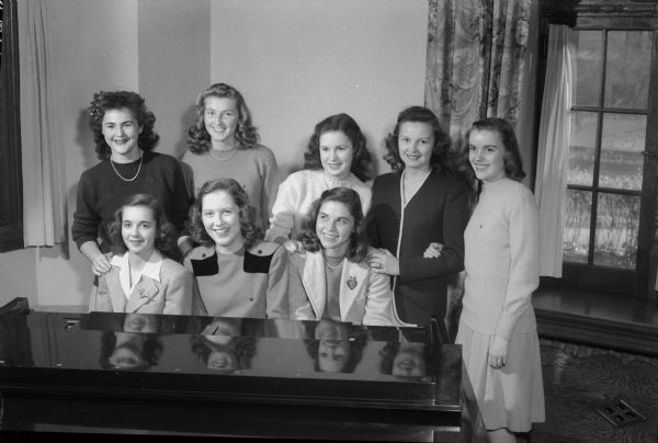 Eight student pledges of Gamma Phi Beta sorority of the University of Wisconsin, gathered for music around a piano. The pledges include, seated: Sally Howell, Fennimore; Ann Dre Schlimgen, daughter of Mr. and Mrs. Lucien Schlimgen, Madison; Ellen Williams, daughter of Mr. and Mrs. C.C. Williams, Madison; standing: Jean Abel, Wisconsin Rapids; Pattie Neilson, Milwaukee; Patricia Sturtevant, Wausau; Joy Wenger, Monroe; and Betty Button, daughter of the Milton Buttons, Madison.