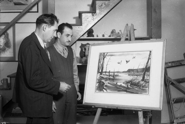 Private Sam Fleischer on the left,of New York City stationed at Truax Field in the radio school, and watercolor artist Byron C. Jorns on the right, standing before a watercolor titled "Mallards Flaring".  The watercolor was painted by Jorns at the U.S.O., and will be sold for the benefit of the Madison Art Association.