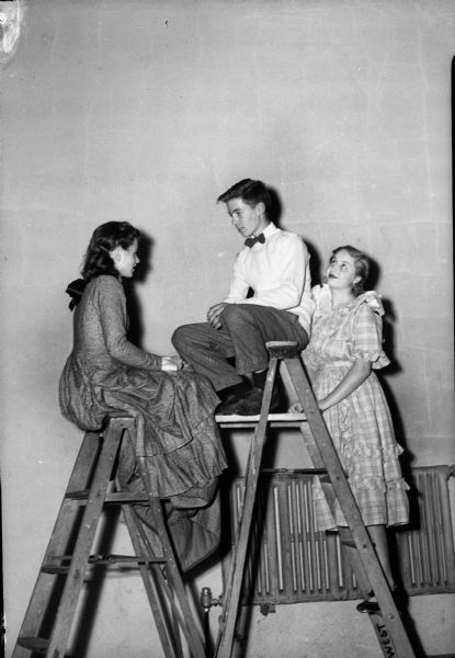 West High School student production of "Our Town" with two actresses and one actor on a ladder. Left to right: Virginia Baldwin, Joel Salter, and Jerry Erickson.