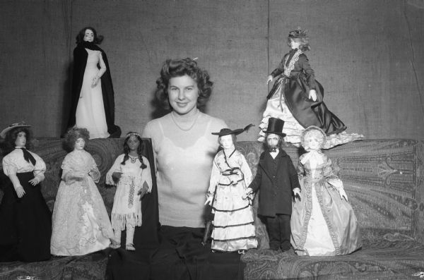 University of Wisconsin freshman Rosemary Bohl posing with eight of the Wisconsin Historical Museum's collection of fashion dolls depicting fashions from the nineteenth century.  The dolls were made by members of Professor Hazel Manning's history of costume course.