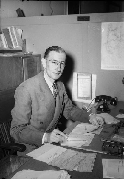 Harry G. Marsh, passenger agent for the Chicago & Northwestern Railroad, seated at his desk. Mr. Marsh was responsible for troop movements to and from Truax Field and the Naval Training School on the University of Wisconsin campus during World War II.