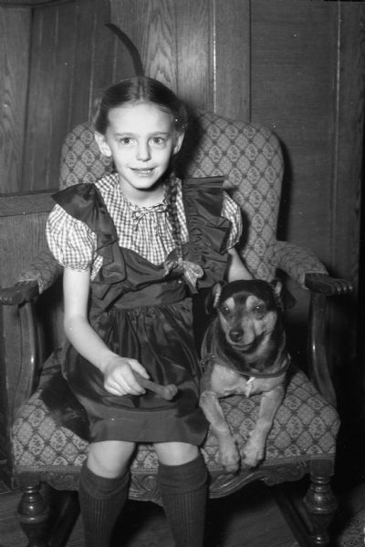 A young girl (possibly the daughter of Russell B. Pyre) dressed in a pinafore with her dog.