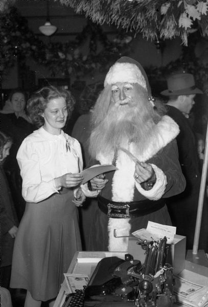 Woman buying a war bond from Santa Claus, who was helping other Manchester employees wait on crowds of purchasers at the bonds-only sale on the store's main floor. Santa Claus is really Fred Claus who lives above the St. Nicholas Cafe, 120 West Main Street.