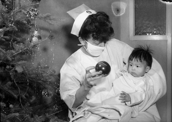 Mrs. Margaret Horstmeier, nurse's aide at Methodist Hospital, shows a Christmas tree ornament to infant John Monegar.