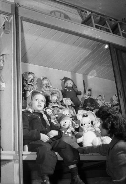 Ellen Jenson, daughter of Mr. and Mrs. Gerhardt Jenson, Edgerton, with store clerk, Jeannine Butler, in the doll section of the toy department at Wolff-Kubly & Hirsig.