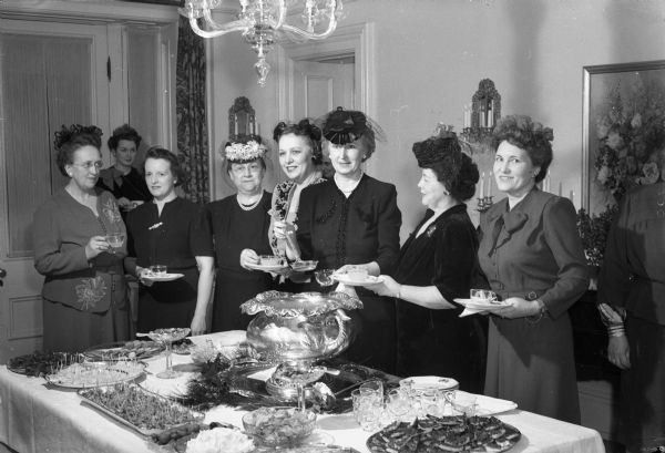 Friends and guests at the Goodland reception including: Mrs. Robert C. Eby, Mrs. M.F. Cooley, Mrs. Paul Irwin, Mrs. Oscar Toebaas, Mrs. Gordon Nelson, Mrs. June B. Wheeler, and Mrs. Francis Lamb. They are standing around the reception table at the Governor's residence, 130 E. Gilman Street.