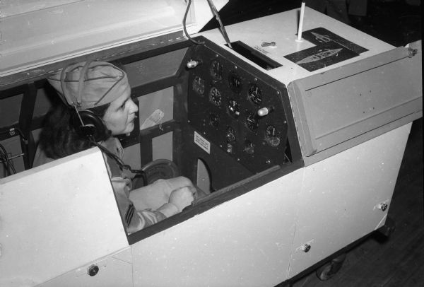 Sgt. Lois Burmeister at the controls of an ambulatory trainer which permits blind flying by instrument instruction by the Civil Air Patrol.