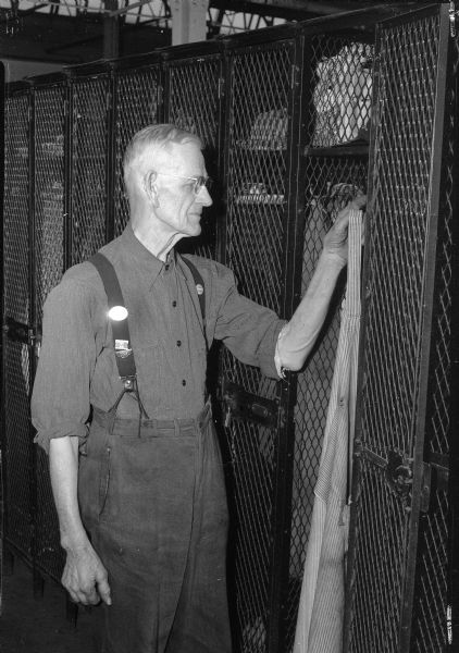 Ira Cole, Gisholt employee for forty-six years, standing at his locker in his work clothes as he retires from work.