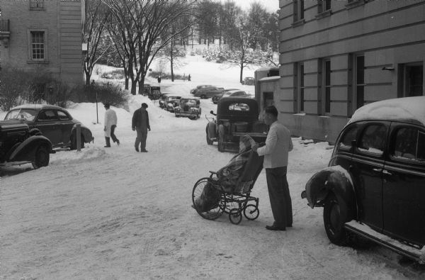 Patient in wheelchair being taken outdoors in the snow between two buildings at Wisconsin General Hospital.