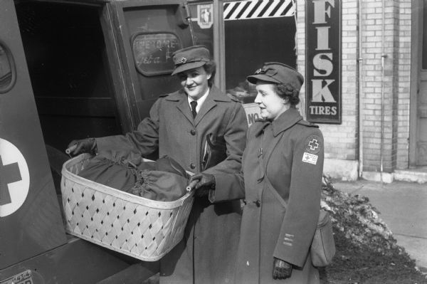 Red Cross Motor Corps workers, Mrs. John (Marjorie) Haley and Mrs. E.W. (Thelma) Nystrom, loading a large basket of Navy kits into a truck to await distribution to service men.