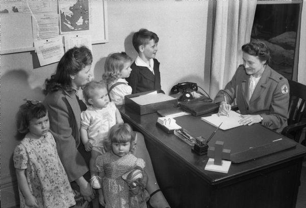Mrs. Kenneth (Rachel) Shiels, a Red Cross liaison agent who works with servicemen and their families, is shown with Mrs. Elvin (Edna) Olson, whose husband, Pvt. Elvin Olson, was killed in the war. Also shown are her five children, Sandra, Carol, Nancy, Sylvia, and David.