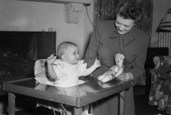 Mrs. Frank R. (Evelyn) Horner standing with her granddaughter, Martha Kerr, who is sitting in a play table.