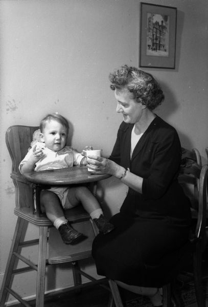 Mrs. Robert J. (Irene) Connor feeding her grandson, Michael Paige, in his highchair.