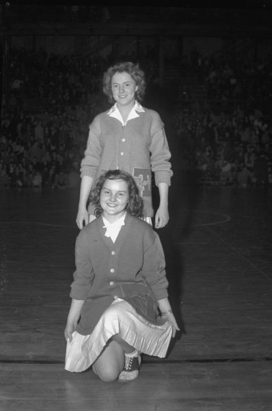 Joyce Burroughs, standing, and Lucille Baker, kneeling, cheerleaders for the Tomah High School team competing in the annual state basketball tournament.