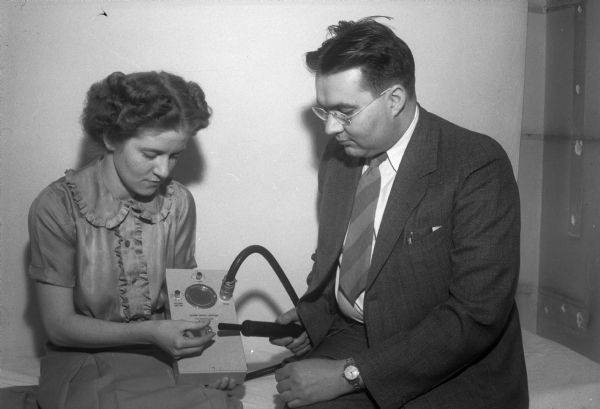 Hulda Gieschen and Dr. Warren E. Gilson, who specializes in electro-physiology and medical electronics at the University of Wisconsin, are looking at a Gilson Metal Locator, made by the Burdick Corp in Milton, Wisconsin, which will detect schrapnel and bullets in wounded soldiers.