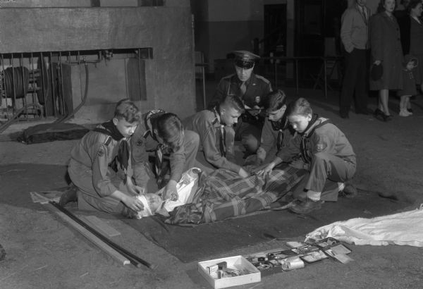 Group portrait of five Boy Scouts with a troop leader teaching them first aid.