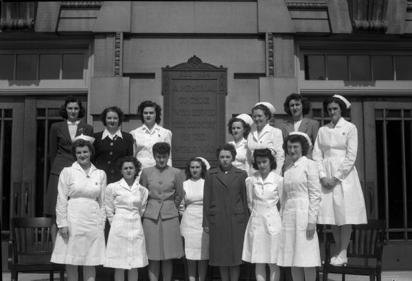 Fifteen nurses from Wisconsin General Hospital, who are entering military service, standing in front of a plaque reading: "1920-1924 A memorial to those who served their country in the World War."