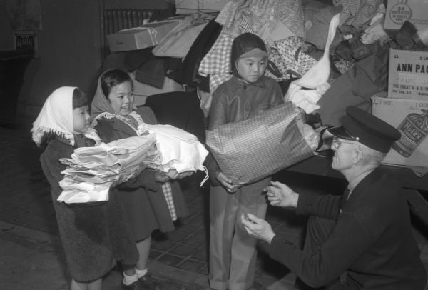 Handing over bundles of clothing collected for the United National Clothing Drive are three Chinese children, Judy, Betty and Billy Lee, children of Mr. and Mrs. George Lee, 413 Fitch Court. They are handing the bundles to Capt. Roy B. Herring at Fire Station No. 4 for distribution to needy families overseas.