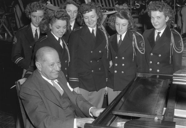 Composer Sigmund Romberg at the piano during an impromtu concert at Central High School. Members of the high school band looking on are, left to right: Beverly Evans, Pat Random, Lois Pease, Marian Taugoff, Joan Miller, and Norma Keating.