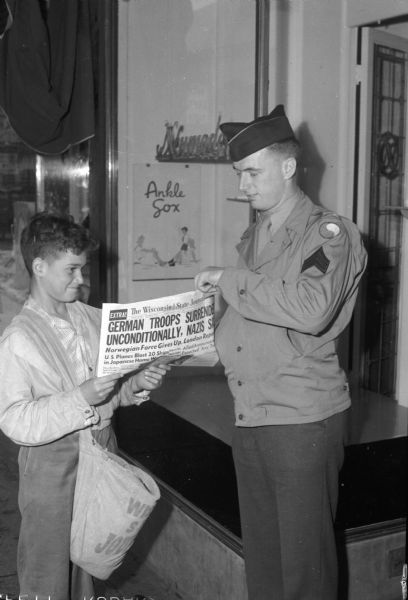 Tom Miller, of 1815 Vilas Avenue, a newsboy for the "Wisconsin State Journal," selling an "extra" edition of the newspaper to Sgt. Ralph Jacobson, announcing the surrender of German troops. Jacobson was wounded in Germany.