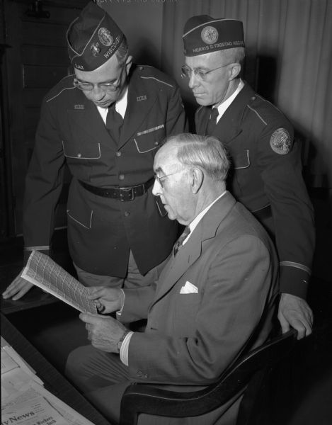 Madison Disabled American Veterans (DAV) officials, Mark R. Kilp, left, Adjutant G. Earl Heath, center, and right, Postmaster Walter J. Hyland inspect a sheet of "Win the War" three-cent stamps first placed on sale July 4, 1942.