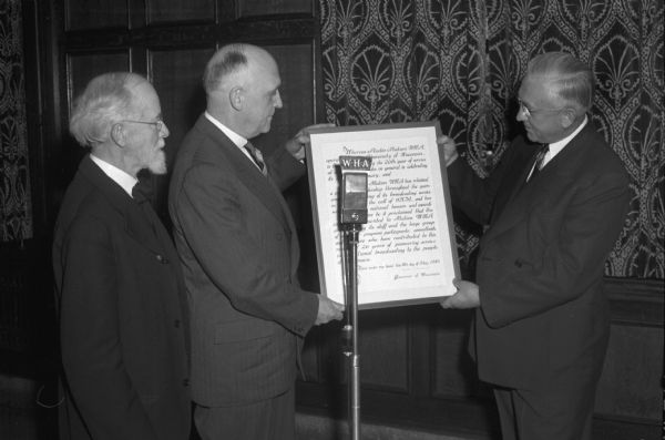 Lieut. Governor Oscar Rennebohm (on right), presenting a citation for twenty-six years of on-air service for radio station WHA to University of Wisconsin President, Edwin B. Fred (center), with WHA's first program director, Prof. William H. Lighty (on left), looking on.