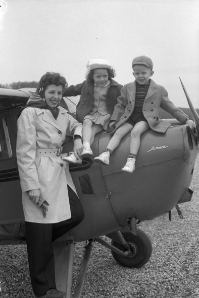 Mrs. F.V. Burcalow is shown with her two children, Vicki and Larry, with an airplane. Mrs. Burcalow is learning how to fly while her husband, an assistant professor of agronomy at the University of Wisconsin, is on leave and doing work for the American government in Italy.