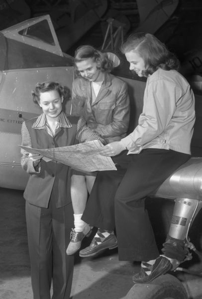 Martha Akin from Phoenix, Arizona, Audrey Waldschmidt, Bismarck, North Dakota, and Helen Harger, Pontiac, Michigan, are shown plotting a course for a flight in Wisconsin.  The three coeds completed the requirements for their private pilots' licenses.