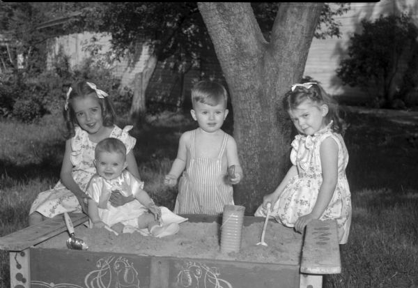 Children of Mr. and Mrs. Norman E. Dean, 909 Lincoln Street, playing in their sandbox. Pictured left to right: Carol 7, holding her baby sister, Derilyn 2 months; Norman Edward (Ned) 2; and Alice 5.