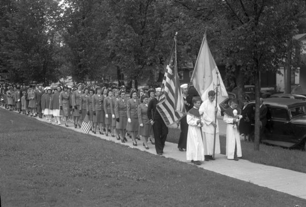A Corpus Christi procession in front of St. Mary's Hospital, including four navy men as canopy bearers, two navy men were flag bearers, and candle bearers were Truax Field soldiers. Nurses in uniform are followed by other nurses in capes, and a crowd of 2,000 people also participated.