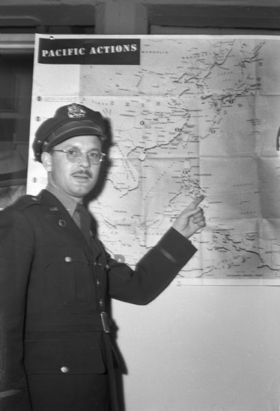 Marine Robert M. Crabb pointing to Japan on a map. He was home in Madison after serving as a war correspondent and being a prisoner of war for three years in Japan.