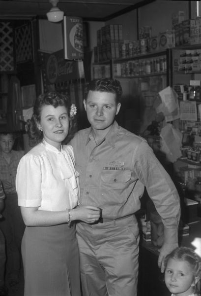 Pfc. William L. Clapp, 2633 Milwaukee Street, with his girlfriend, Virginia Brown. Pfc. Clapp has just returned home from Camp Grant in Rockford, Illinois. A young girl is standing in the right foreground.