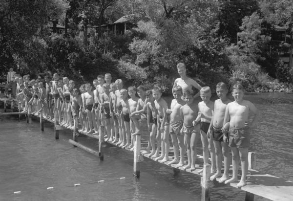 Large group of boys standing in a line on a pier at YMCA Camp Wakanda on Lake Mendota.