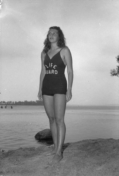 Portrait of Nancy Keenan standing on a beach in a lifeguard swimming suit.  She is one of 7 women lifeguards out of a group of 19 who patrol the Madison beaches for the Madison Parks Department.