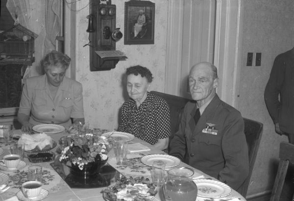 Vice-Admiral Marc A. Mitscher sitting at the dining room table waiting for breakfast to be served to him, his wife Frances Smalley Mitscher (left), and mother, Mrs. O.A. Mitscher (center), at the home of Mrs. Helen Pinch, a sister of his mother.