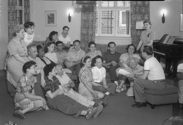 Group of adults listening to a lecturer, probably Dr. Philip S. Fonert talking on American history. The Abraham Lincoln School for Social Science of Chicago, Illinois, sponsored a Summer Institute in Madison for several summers, including 1945. The students who attended the two week sessions were mostly adult union workers and their families.  They lived in rooming houses on Langdon Street and Lake Lawn Place, attended lectures and participated in recreational activities. The photographs show the teachers with groups of students, both indoors and out-of-doors, the students participating in recreational activities such as boating and badminton and the children with a day care worker.<br>The School was run by former University of Wisconsin Associate Professor of Classics Alban D. Winspear. Their textbook was called "Why Work for Nothing" espousing Marx's theory of value. The school had a communist / leftist philosophy and was often confused with the University of Wisconsin's School for Workers.</br>