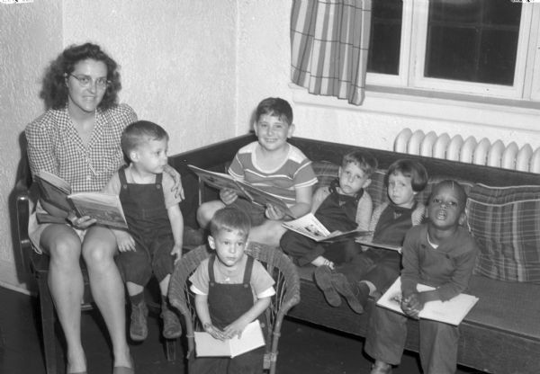 Six children with a day care worker. The Abraham Lincoln School for Social Science of Chicago, Illinois, sponsored a Summer Institute in Madison for several summers, including 1945. The students who attended the two week sessions were mostly adult union workers and their families. They lived in rooming houses on Langdon Street and Lake Lawn Place, attended lectures and participated in recreational activities. The photographs show the teachers with groups of students, both indoors and out-of-doors, the students participating in recreational activities such as boating and badminton and the children with a day care worker. The School was run by former University of Wisconsin Associate Professor of Classics Alban D. Winspear. Their textbook was called "Why Work for Nothing" espousing Marx's theory of value. The school had a communist / leftist philosophy and was often confused with the University of Wisconsin's School for Workers.