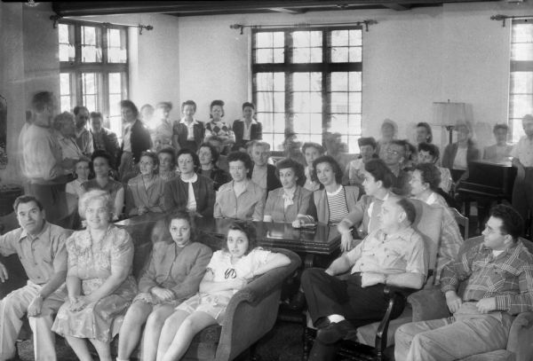 Group of students listening to a lecture. The Abraham Lincoln School for Social Science of Chicago, Illinois, sponsored a Summer Institute in Madison for several summers, including 1945. The students who attended the two week sessions were mostly adult union workers and their families. They lived in rooming houses on Langdon Street and Lake Lawn Place, attended lectures and participated in recreational activities. The photographs show the teachers with groups of students, both indoors and out-of-doors, the students participating in recreational activities such as boating and badminton and the children with a day care worker. The School was run by former University of Wisconsin Associate Professor of Classics Alban D. Winspear. Their textbook was called "Why Work for Nothing" espousing Marx's theory of value. The school had a communist / leftist philosophy and was often confused with the University of Wisconsin's School for Workers.
