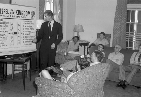 Students listening to Rev. Claude Williams teaching "Religion in Contemporary Society." The blackboard says "Gospel of the Kingdom: The Gospel to the Poor, Good News to the Poor" with bible references. The Abraham Lincoln School for Social Science of Chicago, Illinois, sponsored a Summer Institute in Madison for several summers, including 1945. The students who attended the two week sessions were mostly adult union workers and their families. They lived in rooming houses on Langdon Street and Lake Lawn Place, attended lectures and participated in recreational activities. The photographs show the teachers with groups of students, both indoors and out-of-doors, the students participating in recreational activities such as boating and badminton and the children with a day care worker. The School was run by former University of Wisconsin Associate Professor of Classics Alban D. Winspear. Their textbook was called "Why Work for Nothing" espousing Marx's theory of value. The school had a communist / leftist philosophy and was often confused with the University of Wisconsin's School for Workers.
