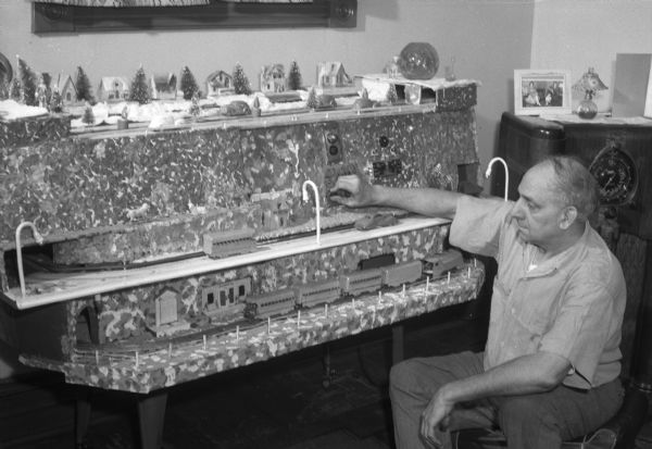 August Carsten, a builder of one of the few roll-away model trains and villages in the country, is shown at the main control of the electric operated model.