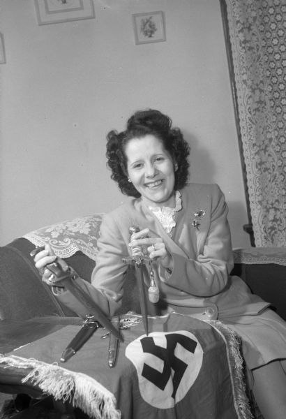 Mabel Pendleton is shown holding German knives with a German flag on a table. The items, retired from service, were sent by her son, Sgt. Frederick N. Hallway, from France where he had been stationed with the Third Army.