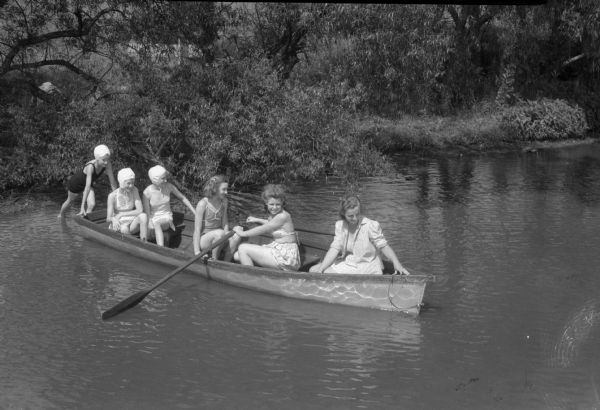 Girls scouts boating on Lake Katrina at Camp Brandenburg near Springfield Corners. Pictured pushing the rowboat is Mary Lou Steinike. In the rowboat from left to right: Geraldine Larson, Betty Ogden, Marilyn Jones, Mary Waters, and waterfront counselor Catherine Conlin.