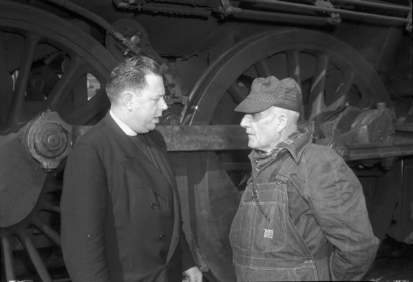 A priest (Father Aloin R. Kutchera from St. Paul's University Chapel?) with a railroad worker standing next to a locomotive.