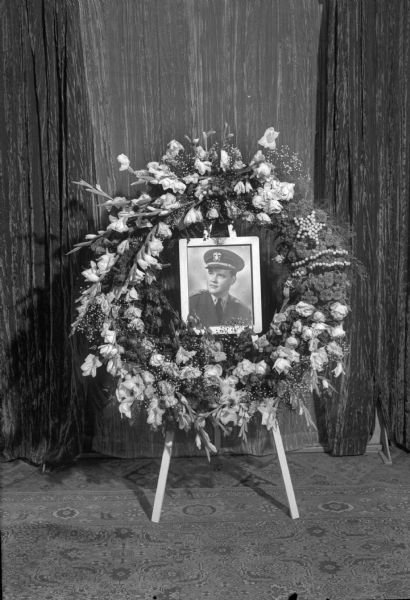 Funeral wreath with photograph in center of Lieut. William T. Gleason, at Lieut. Gleason's funeral service held on July 27, 1945, at St. Bernard's Church. Lieut. Gleason was a veteran of the Royal Canadian Air Force and the U.S. Army Air Force. He was killed in a mid-air collison with another airplane over Tacoma, Washington.