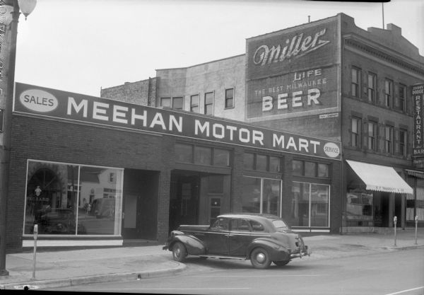 Exterior view of Meehan Motor Mart, 209 East Washington Avenue, and the Jimmy Dodge Restaurant, 203 East Washington Avenue, and the H.F. Sharratt and Company-Auctioneers, 205 East Washington Avenue. Meehan Motor Mart is the authorized Packard automobile sales and service dealer in the Madison area, and a Packard is parked in front of the building.