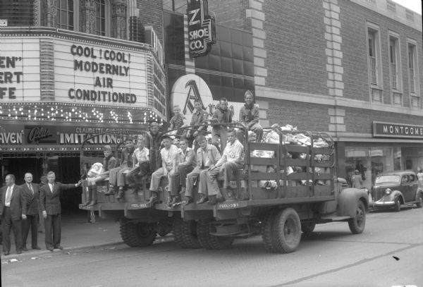 Members of the Junior Red Cross, Boy Scouts of Troops 20 and 30, and boys of Madison, sitting on the back of a Truax Field army truck loaded with waste paper which was collected to raise money for the Junior Red Cross. The truck is parked on State Street in front of the Capitol Theatre. Children who participated in the paper drive were able to attend a free movie at the Capitol Theatre.