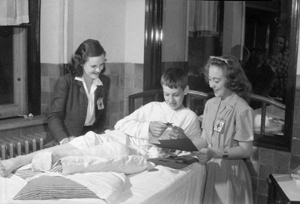 Junior Red Cross members making Christmas tree decorations for military service units and hospitals overseas. Arline Whitefoot, on the right, assists a young patient at the Wisconsin Orthopedic Hospital, 435 Randall Avenue, under the supervision of Margaret Kennedy.